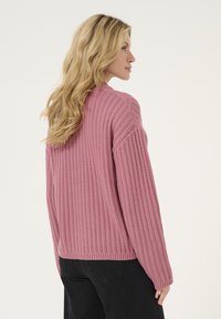 Pink ribbed sweater with long sleeves and a relaxed fit, featuring textured knit, round neckline, and a straight hem.