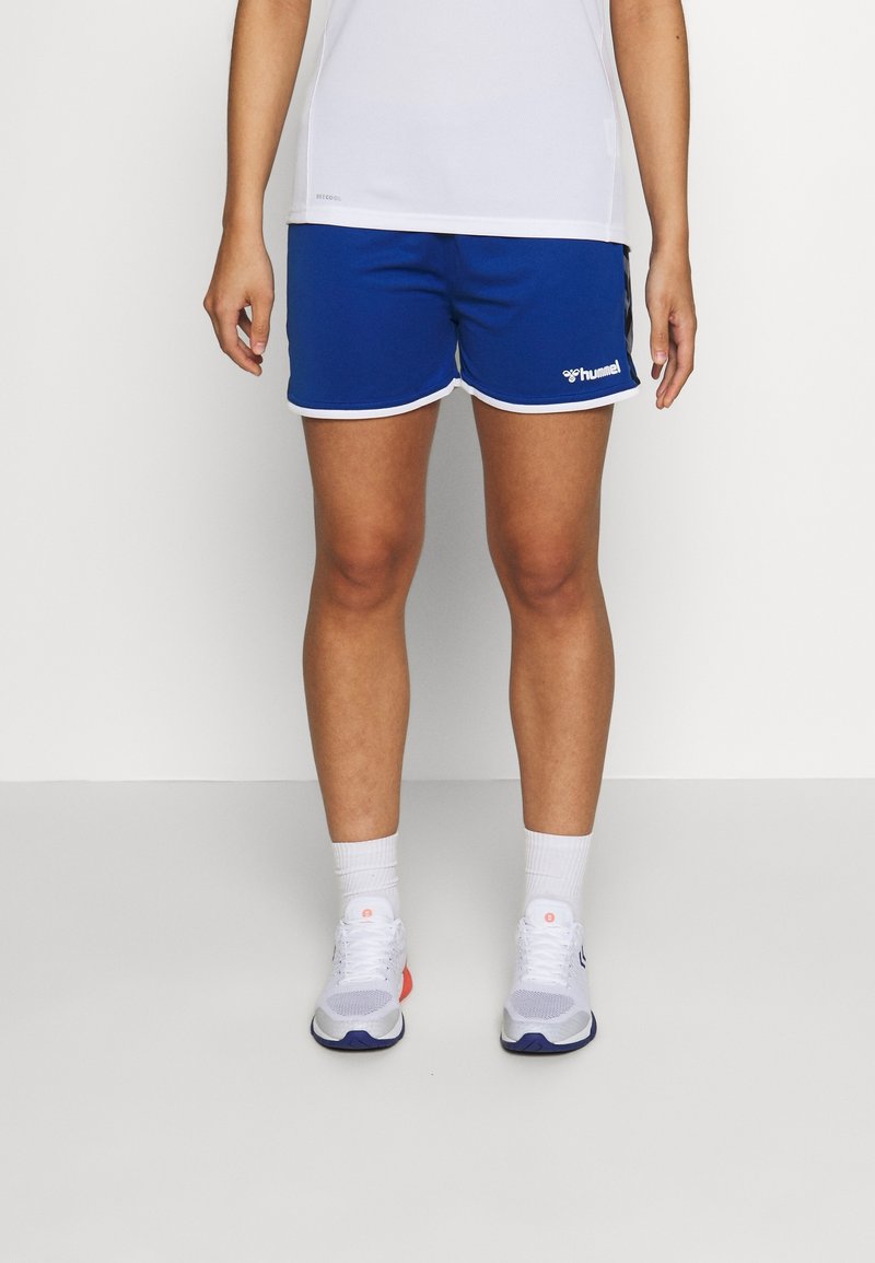 Blå sportshorts med vit kant och logotyp, tillverkade av lättviktig tyg, kombinerade med vita strumpor och sneakers. Enkel design, knä-lång.
