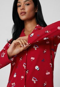 Rode langemouwen hemd met een speelse feestdagenprint met feestelijke motieven. Gemaakt van zachte stof met een gestructureerde kraag en knoopmanchetten.