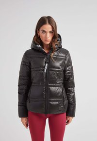 Svart puffer-jacka med en glänsande, quiltad design, elastiska manschetter och dragkedja fram. Inkluderar en huva med kontrasterande foder.