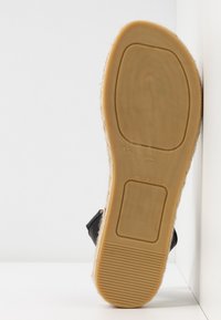 Semelle de sandale noire avec une surface en caoutchouc texturé couleur tan ; présente un bord en jute sur le contour ; taille 39 ; marqué "FABRIQUÉ EN ESPAGNE."