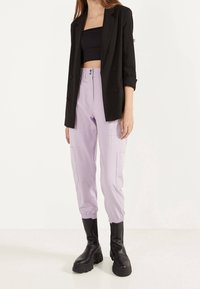 Svart dubbelknäppt kavaj över en svart crop top, matchad med ljuslila cargobyxor och kraftiga svarta stövlar.