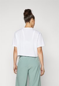 T-shirt bianca cropped realizzata in morbido cotone. Presenta maniche corte e un collo rotondo. Abbinata a pantaloni con vestibilità rilassata di un verde chiaro.