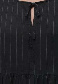 Μαύρο φόρεμα με λεπτές λευκές κάθετες ρίγες, λαιμόκοψη με άνοιγμα και υφασμάτινο φιόγκο και λεπτομέρεια στη μέση με ρυτίδες.