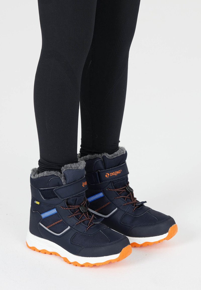 Nassblaue wasserdichte Stiefel mit orangefarbenen Akzenten, Futter aus Fell und multifarbigem Textil. Mit Klettverschlüssen und einer strukturierten Gummisohle.