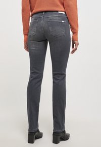 Jeans gris oscuro con un corte ajustado, diseño de cinco bolsillos y un sutil detalle de costura en la parte trasera. Combinados con botas de tacón negras.