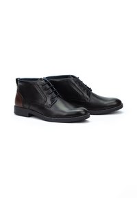 Botas de tobillo de cuero negro con un acabado suave, con cordones azules, acentos en el tacón marrón en contraste y una suela cosida para mayor durabilidad.