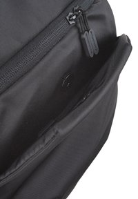 Interior de una bolsa de tela negra con una textura suave, que cuenta con un cierre de cremallera y un pequeño bolsillo con botón a presión.