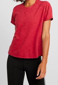 Röd t-shirt med korta ärmar som har en rundad halsringning, något strukturerad tyg och sidoflikar vid fållen för bättre passform och komfort.