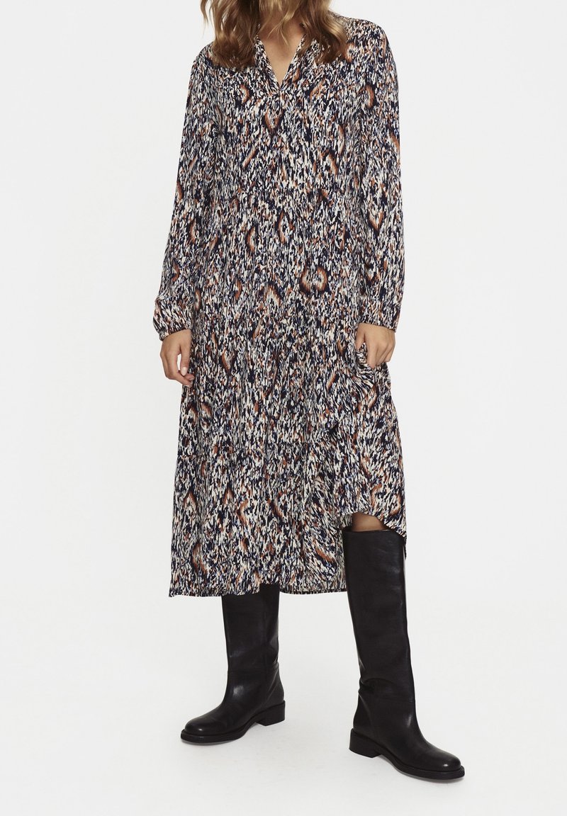 Lång, tryckt klänning i en blandning av marinblått, krämfärgat och rostfärgat med v-ringning, långa ärmar och dolda sidofickor. Bärs med svarta knähöga stövlar.