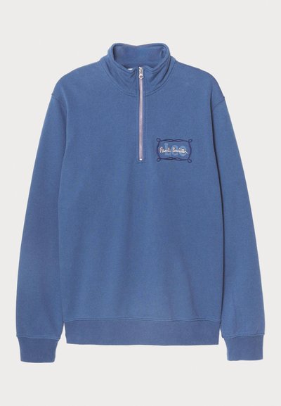 Plavi dukserica sa visokim ovratnikom i polu-rajserom. Izvezeni detalj s logotipom na lijevoj strani prsnog koša, a rebrasti manžetni i donji rub. Mekana pamučna mješavina.