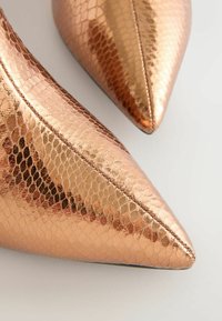 Chaussures à bout pointu en or rose métallisé, présentant un motif en cuir de serpent texturé avec une finition brillante et des détails de couture visibles.