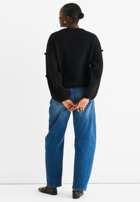Black textured sweater with oversized sleeves, paired with light blue loose-fitting jeans and black flats. Accessories include hoop earrings.