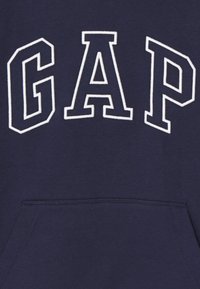 Felpa blu navy con tasca a marsupio, caratterizzata da grandi lettere bianche ricamate "GAP" sulla parte anteriore. Materiale morbido e design casual.