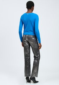 Suéter azul brillante hecho de material suave, combinado con pantalones plateados brillantes de corte ajustado y dobladillo deshilachado, y botas de tacón alto negras.