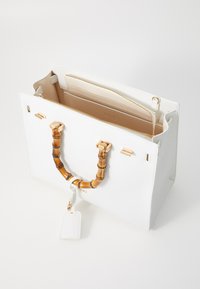 Witte handtas met een bamboe handvat, gouden accenten en een georiënteerd interieur met compartimenten in een tan kleur. Label bevestigd.