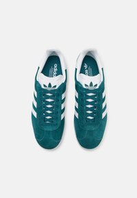 Suede sneakers in dark teal with white stripes and laces. Features a padded tongue, branding on the tongue, and a textured rubber sole.