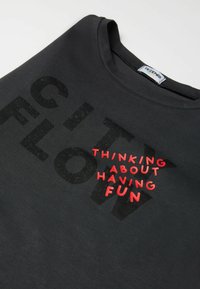 Schwarzes T-Shirt mit großen schwarzen Buchstaben "CITY FLOW" und rotem Text "DARÜBER NACHDENKEN, SPASS ZU HABEN." Aus weichem, glattem Stoff mit Rundhalsausschnitt.