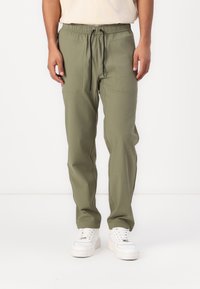 Groene sportbroek met een elastische tailleband en zwarte trekkoord, voorzien van twee zijzakken en een slim fit ontwerp.