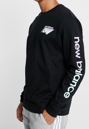 Camiseta negra de manga larga con un logo gráfico multicolor en el pecho y texto "new balance" a lo largo de la manga. Material de algodón.