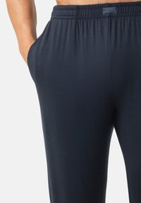 Marineblauwe broek met een losse pasvorm, elastische tailleband en zijzakken, gemaakt van een zachte, gladde stof met een lichte textuur.