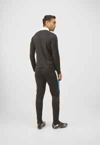 Chándal atlético negro de manga larga y pantalones, con acentos en verde y azul en los lados, hecho de una tela suave y elástica.
