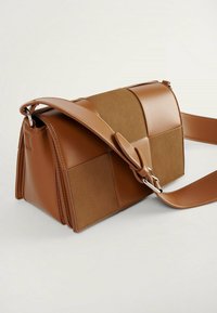 Bolso de mano en cuero y ante marrón con un diseño geométrico, forma cuadrada, correa ajustable y detalles en hardware plateado.