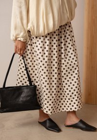 Šviesiai rudos spalvos sijonas su taškeliais ir laisvu siluetu, derinamas su juodu odiniu rankiniu krepšiu ir juodais smailiais mūlais. Sluoksniuotos medžiagos, su subtiliu blizgesiu.