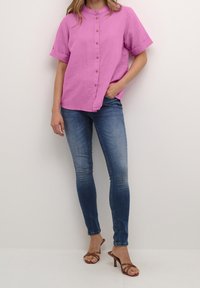 Kortärmad skjorta med krage i livlig rosa färg med bruna knappar, matchad med blå skinny jeans och bruna remsandaler med klack.