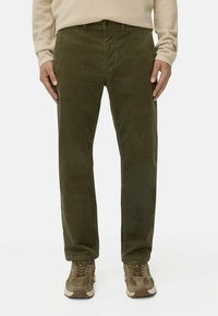 Donkergroene corduroy broek met een rechte snit, voorzien van een knoopsluiting en riemlussen. Gecombineerd met lichtbruine sportschoenen.