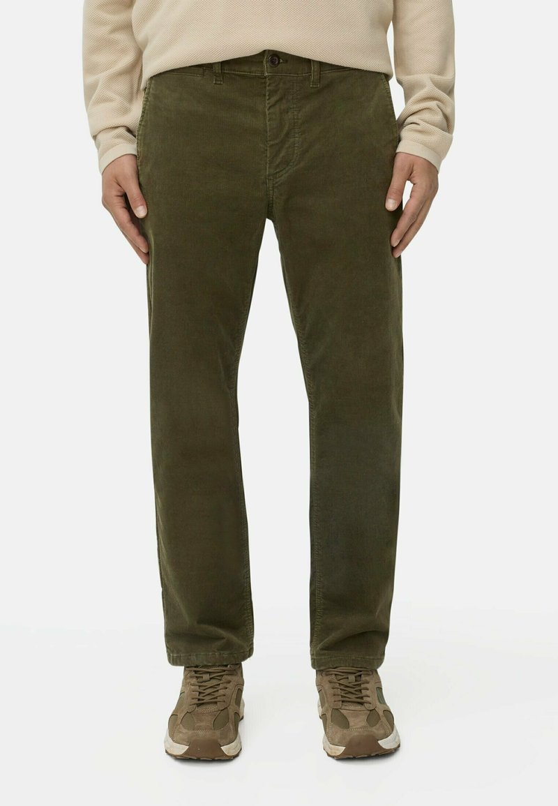 Donkergroene corduroy broek met een rechte snit, voorzien van een knoopsluiting en riemlussen. Gecombineerd met lichtbruine sportschoenen.
