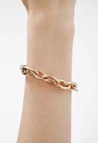 Pulsera de cadena de oro y oro rosa que presenta eslabones ovalados interconectados, textura suave y un acabado pulido, llevada en una muñeca.