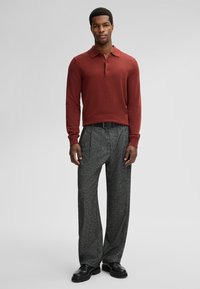 Rode gebreide polo met lange mouwen en gestructureerde grijze broek. Zwarte riem en schoenen maken de outfit compleet. Casual pasvorm met een moderne uitstraling.