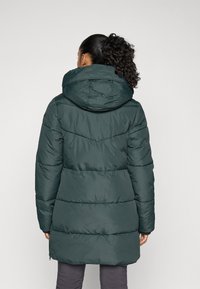 Abrigo acolchado verde con capucha, que presenta un diseño acolchado y costuras verticales. El abrigo tiene un corte de longitud media y puños elásticos.