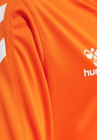 Helles orange Sportshirt mit glatter Textur. Verfügt über ein weißes Logo und Akzente. Design betont die Funktionalität von Sportbekleidung.