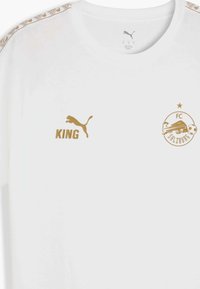 Camiseta blanca de manga corta con logotipos dorados: logotipo de Puma en el lado izquierdo del pecho, texto "KING" y escudo del FC Salzburg. Patrón decorativo a lo largo del hombro.