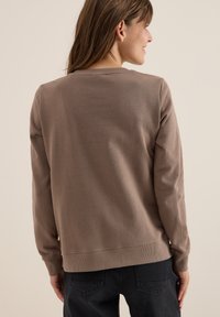 Sweatshirt marron avec un col rond, des poignets et un ourlet côtelés. Le tissu semble doux avec une coupe décontractée. Porté avec un pantalon noir, vu de l'arrière.