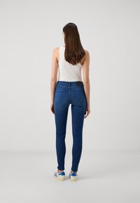 Jeans skinny de color azul oscuro con un ajuste ceñido, que presentan bolsillos traseros y un detalle de cinturilla negra, combinados con zapatos de rayas azules y blancas.