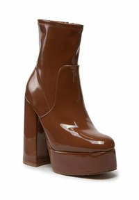 Bota de plataforma marrón brillante con tacón alto y grueso y puntera redonda, diseñada para la moda y el estilo.