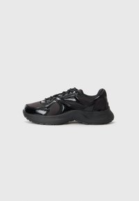 Baskets de sport noires avec un mélange de textures brillantes et mates, fermeture à lacets, semelle de soutien et design épuré.
