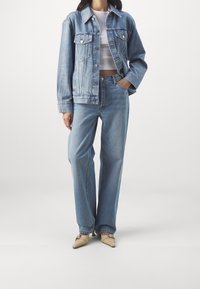 Chaqueta de denim azul claro con un corte relajado, dos bolsillos frontales, combinada con jeans azul claro de tiro alto y zapatos beige de punta.