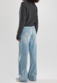 Suéter gris de canalé, de cuello alto, combinado con pantalones vaqueros de pierna ancha en un azul claro con textura desgastada y bolsillos traseros. Calzado casual visible.