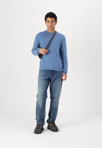 Ljusblå tröja med ribbat halslinne och muddar, tillsammans med blå jeans och svarta sneakers. Modellen bär en svart axelremsväska.