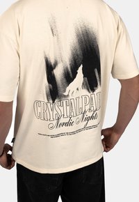 Béžové bavlněné tričko s černou grafikou vlka a textem "CRYSTALPARK Nordic Nights" na zádech. Krátké rukávy, uvolněný střih.