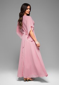 Lång rosa klänning i lätt tyg, med vida ärmar, knytbart midjeband och en svävande silhuett. Avslutad med en slät textur.