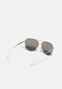 Óculos de sol estilo aviador com lentes cinza escuro, armação de metal prateado e extremidades de acetato brancas. Apresenta almofadas nasais e um design minimalista.