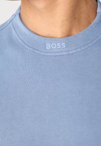 Gros plan d'un t-shirt bleu clair à col rond avec le mot « BOSS » brodé en blanc sur le col, porté par une personne.