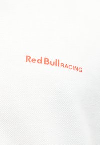 Hvit teksturert stoff med liten rød-oransje "Red Bull Racing"-tekst trykt på skrå på overflaten.