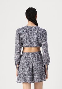 Cvjetni crop top i suknja u tamnoplavoj boji, sa naboranim strukom, napuštenim rukavima i vezicama na otvorima za zapešća. Ukrašen malim ružičastim cvjetovima.