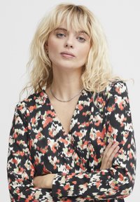 Robe portefeuille noire avec un motif floral vif en rouge, vert et crème, dotée de manches longues et d'un décolleté en V profond.